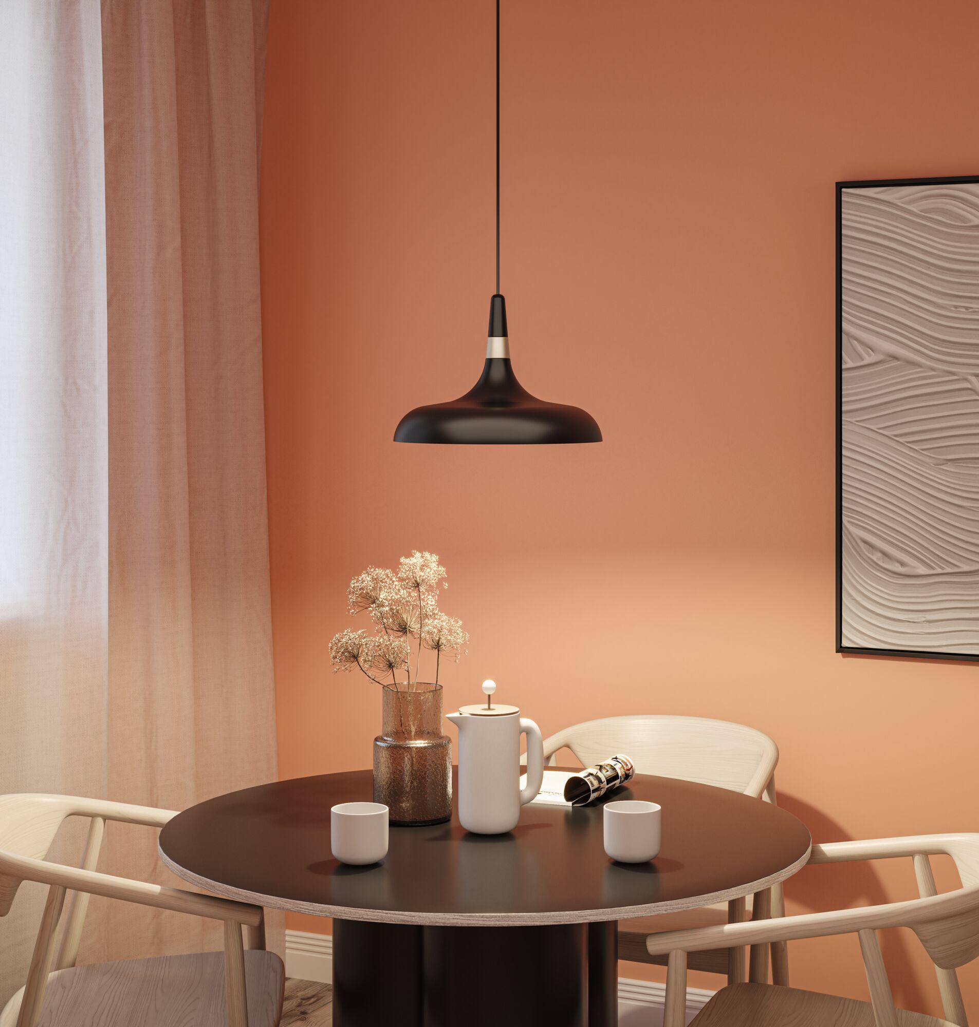 Black metal pendant lamp above round wooden table with ceramic jug and cups in dining room