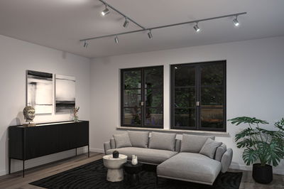 Moderne woonkamer met grijze stoffen bank, zwarte dressoir en verstelbare metalen plafondspots.