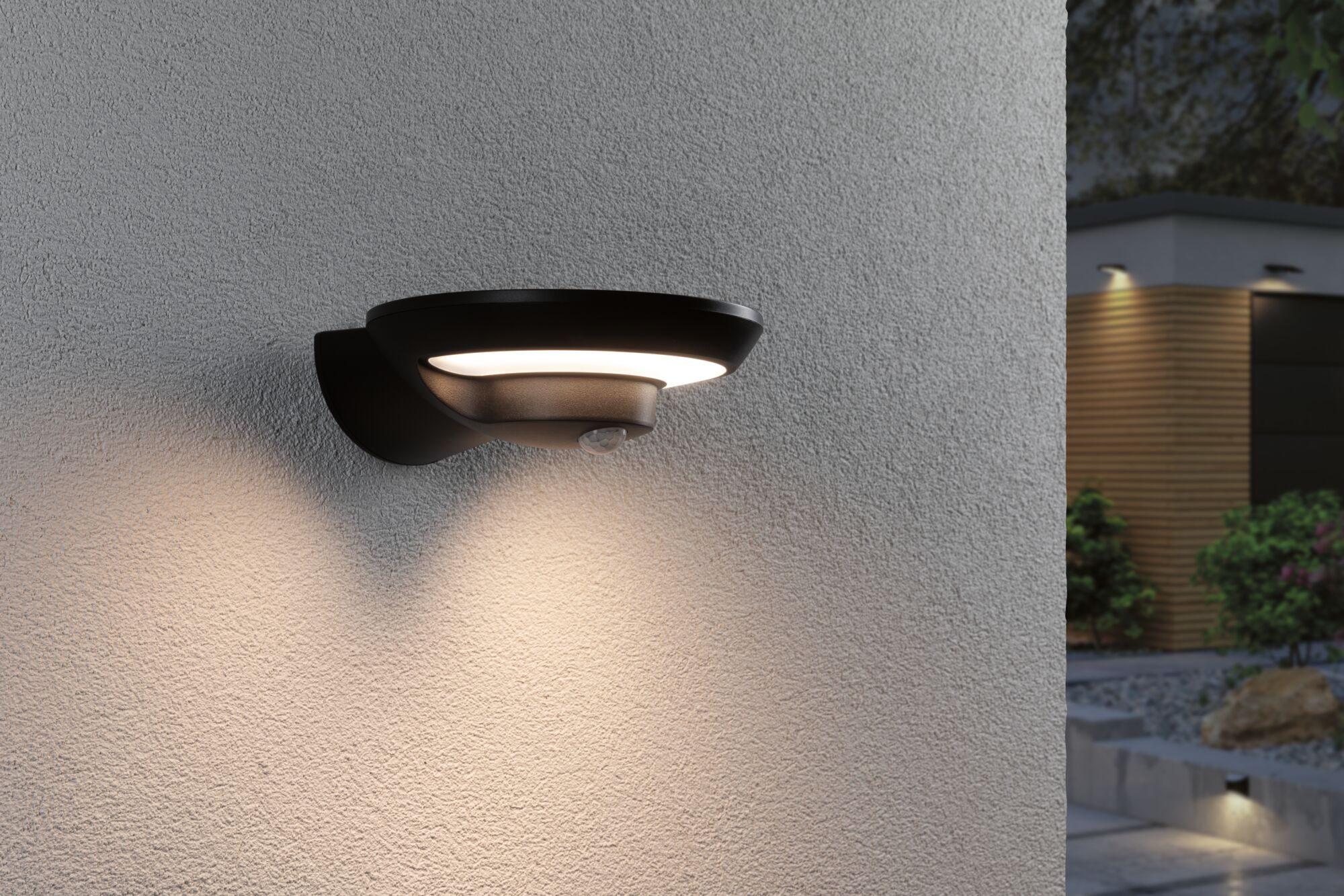 Black outdoor wall light in metal with warm white LED and motion sensor on house wall.