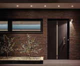 Modern house facade with brown bricks, black door, and energy-saving LED ceiling spotlights outside.