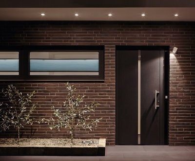 Moderne gevel met bruine bakstenen, zwarte deur en energiezuinige LED-plafondspots buiten.