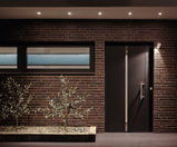 Modern house facade with brown bricks, black door, and energy-saving LED ceiling spotlights outside.