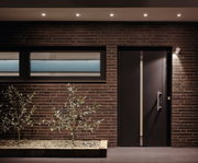 Moderne Hausfassade mit brauner Ziegelwand, schwarzer Tür und LED-Außenbeleuchtung