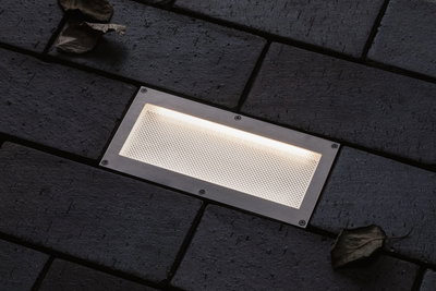 Rectangular stainless steel recessed light with warm white glow in dark pavement for outdoor lighting