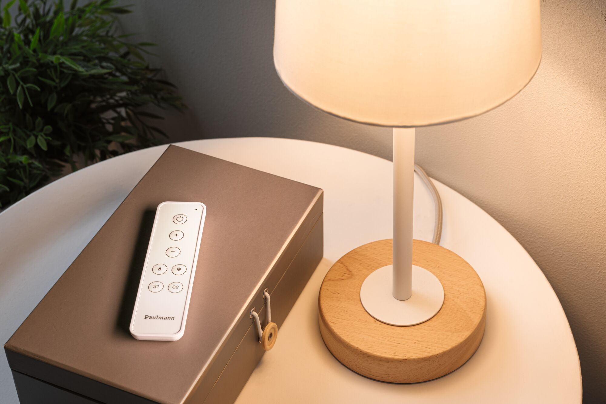 Télécommande blanche sur boîte marron à côté d'une lampe de table avec base en bois et abat-jour blanc pour éclairage LED