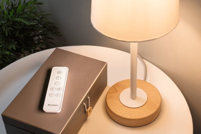 White remote on brown box beside table lamp with wooden base and white shade for LED lighting