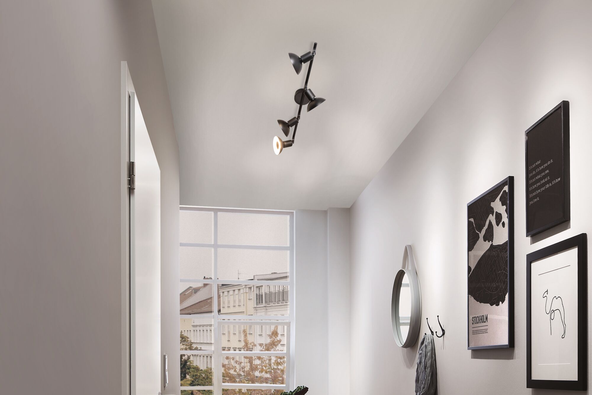 Schwarze Deckenleuchte mit vier verstellbaren Spots in modernem Flur mit Spiegel und Wandbildern.