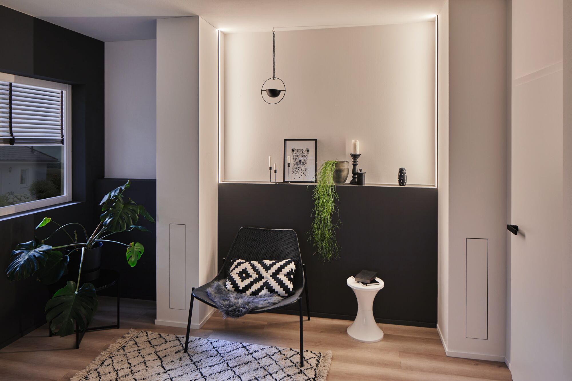 Modern living room with black chair, geometric cushion, plants, and indirect LED wall lighting for ambiance.
