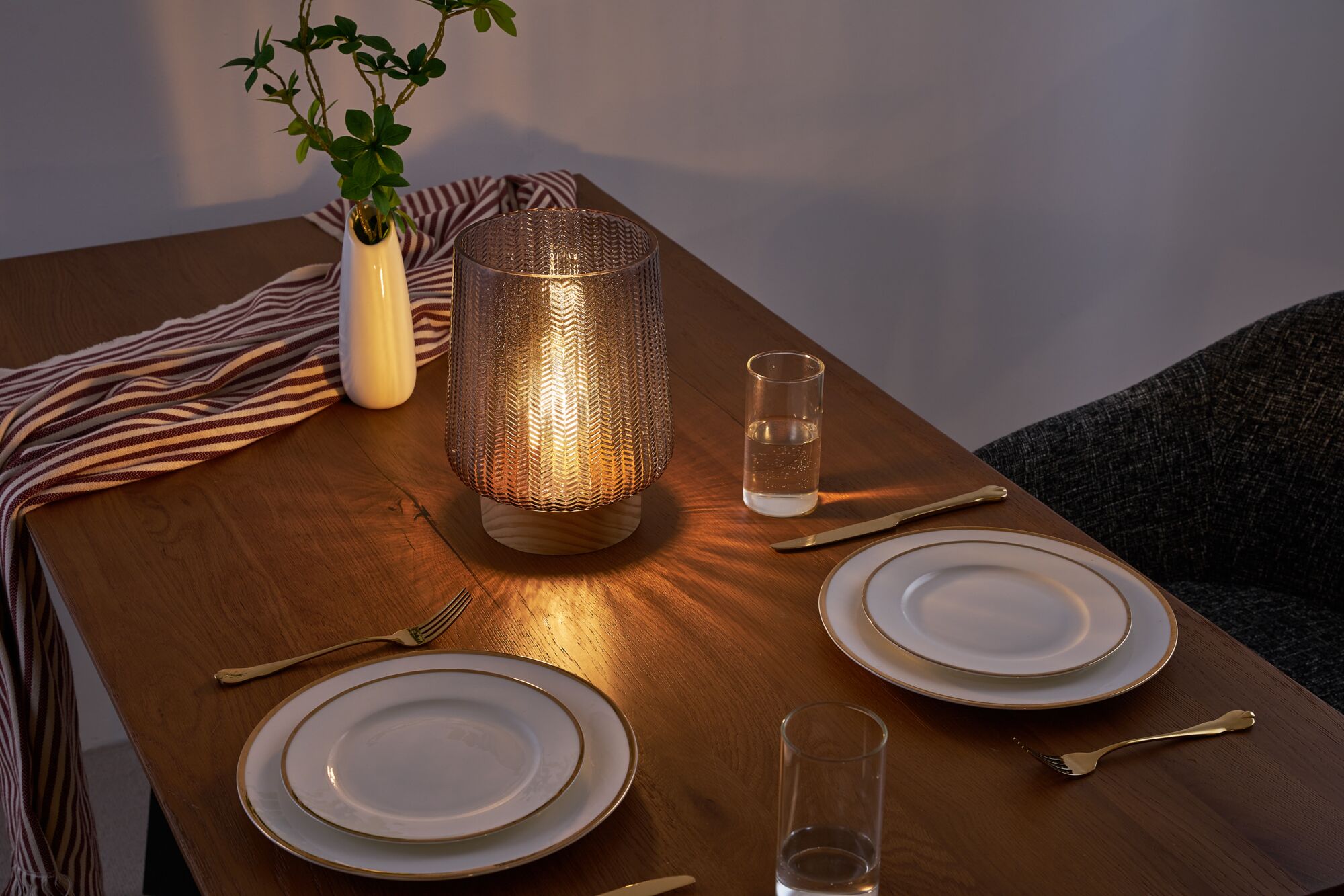 Gezellige eettafel met bruine glazen lamp op houten tafel, wit porselein met gouden rand en gouden bestek