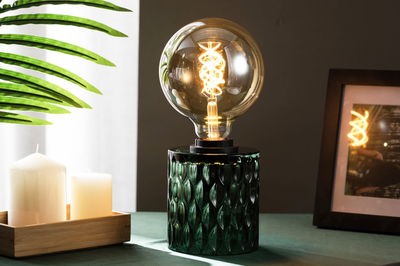 Bordlampe med grøn glasfod og stor pære, der udsender varmt lys til hyggelig belysning