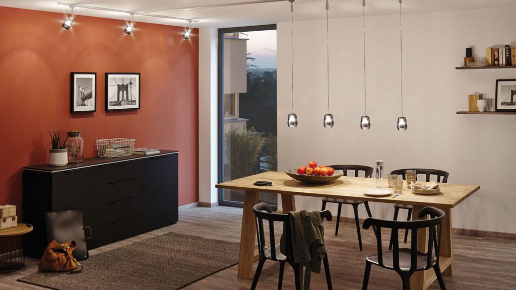 Modern dining room with wooden table, black chairs, and four silver pendant lights hanging above.