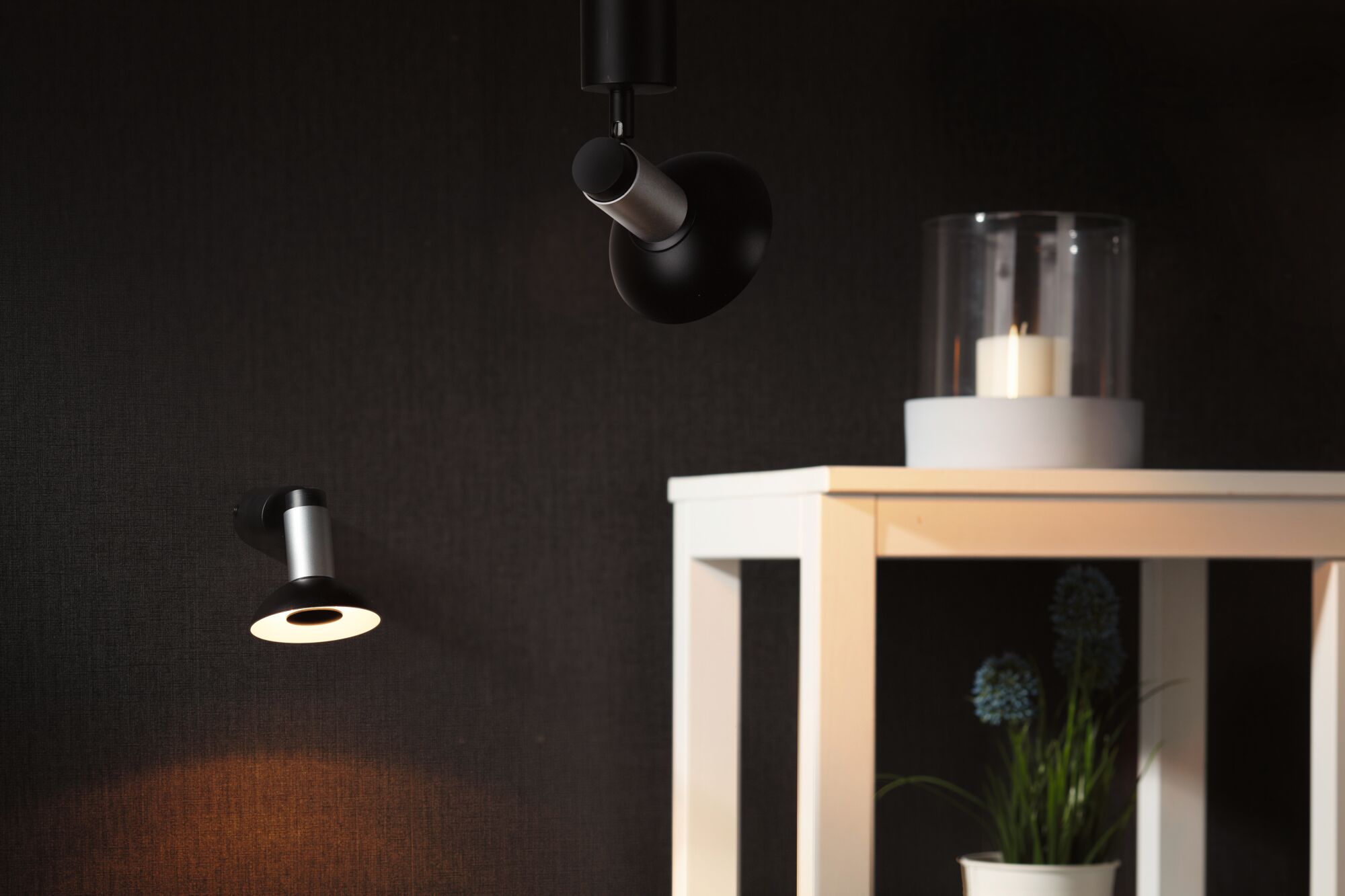Black and silver LED wall and ceiling lights on dark wall with white table and candle decor