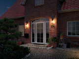 Illuminated house entrance with white glass doors and two black wall lamps on red brick.