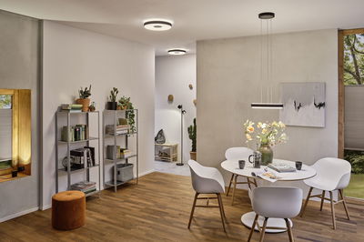 Moderne spisestue med hvidt bord, stole i plastik og træ, LED-loftslamper og pendel.