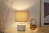 Lampe de table beige avec abat-jour en tissu et base en céramique sur table blanche près de déco et cadre