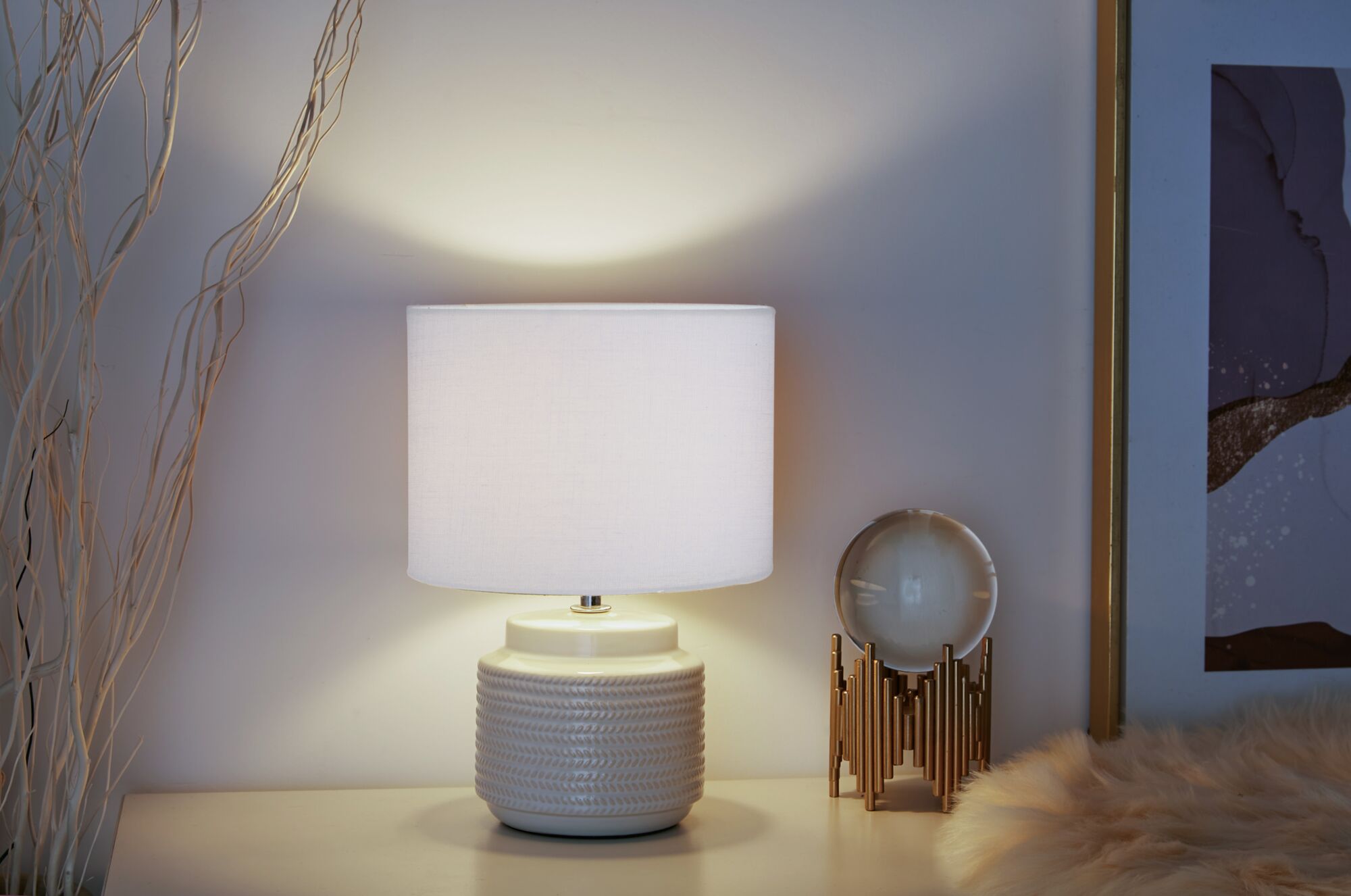Lampe de table beige avec abat-jour en tissu et base en céramique sur table blanche près de déco et cadre