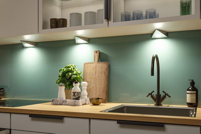 Plan de travail de cuisine moderne en bois avec évier en acier inoxydable et éclairage LED sous les meubles.
