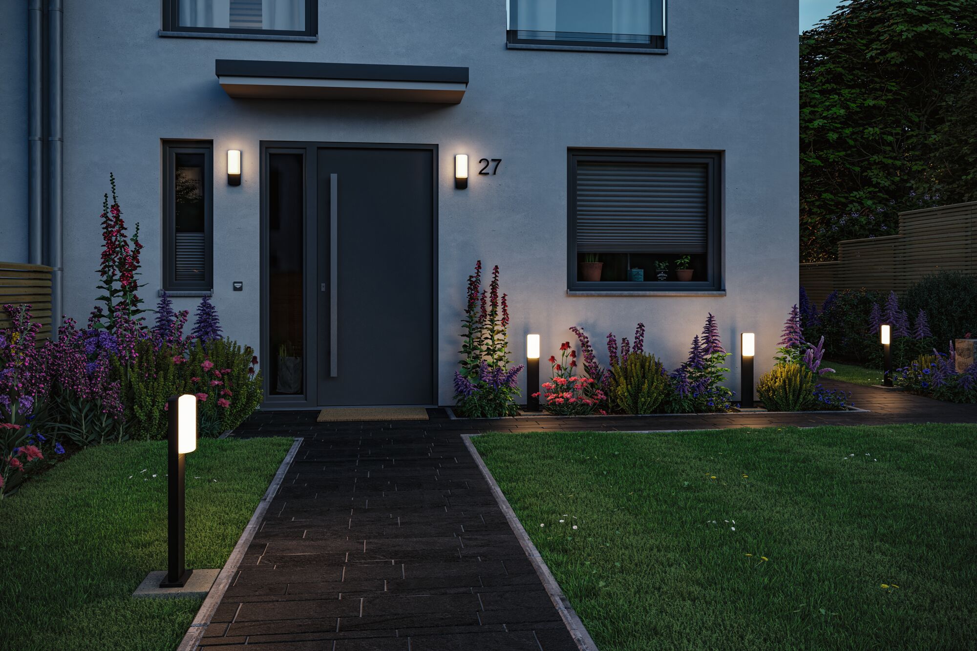 Moderne buitenverlichting met zwarte LED-paalverlichting en wandlampen bij huisgevel en tuinpad.