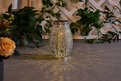Metalllaterne mit filigranem Muster in Silber, erzeugt dekoratives Lichtspiel auf Boden im Garten.