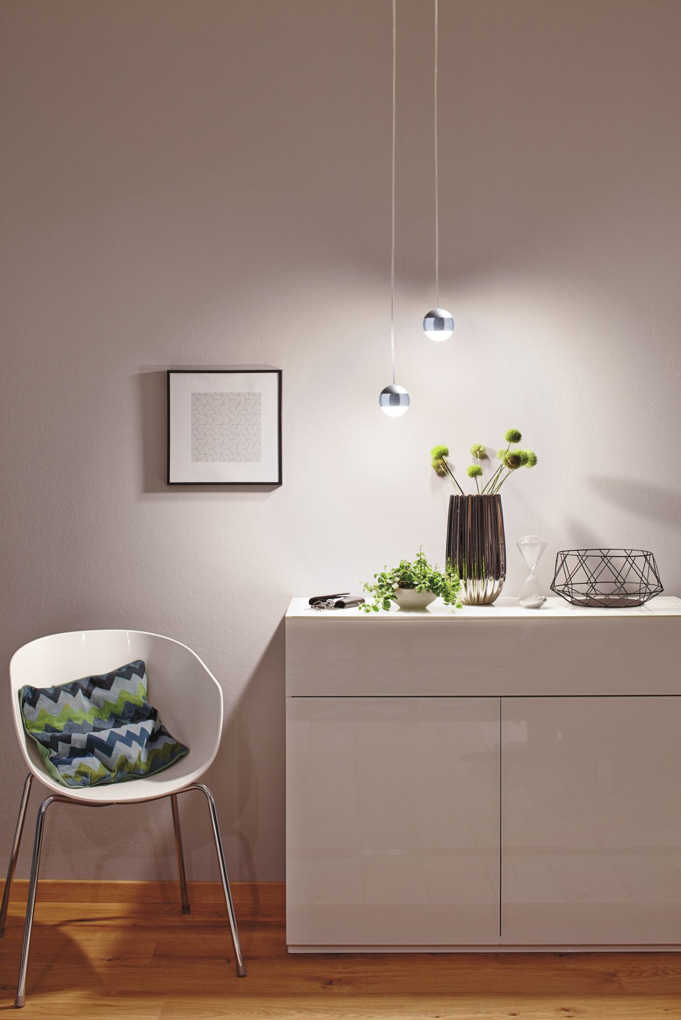 Moderne weiße Hochglanz-Kommode mit Deko und zwei runden LED-Hängeleuchten in warmweißem Licht