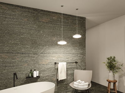 Modernes Badezimmer mit freistehender weißer Badewanne, grauer Natursteinwand und zwei runden LED-Hängelampen.
