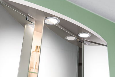 Lumière LED ronde pour miroir de salle de bain avec cadre argenté et armoire intégrée avec étagère en verre.