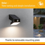 Black solar outdoor wall light with motion sensor mounted on grey wall, energy-saving LED lighting