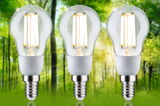 Three clear glass LED bulbs with E14 base in front of green forest background for energy-saving lighting