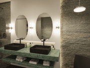 Modern bathroom with green marble countertop and black rectangular stone sinks with oval mirrors.