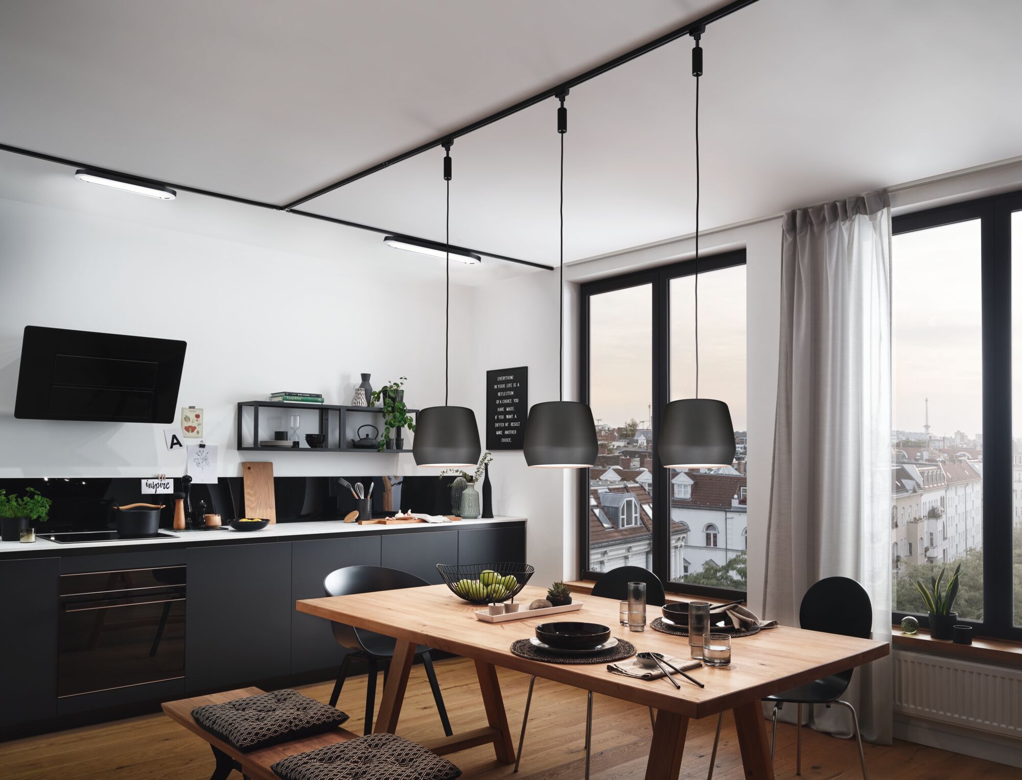 Modern kitchen with black metal pendant lamps over wooden table, large windows and city view