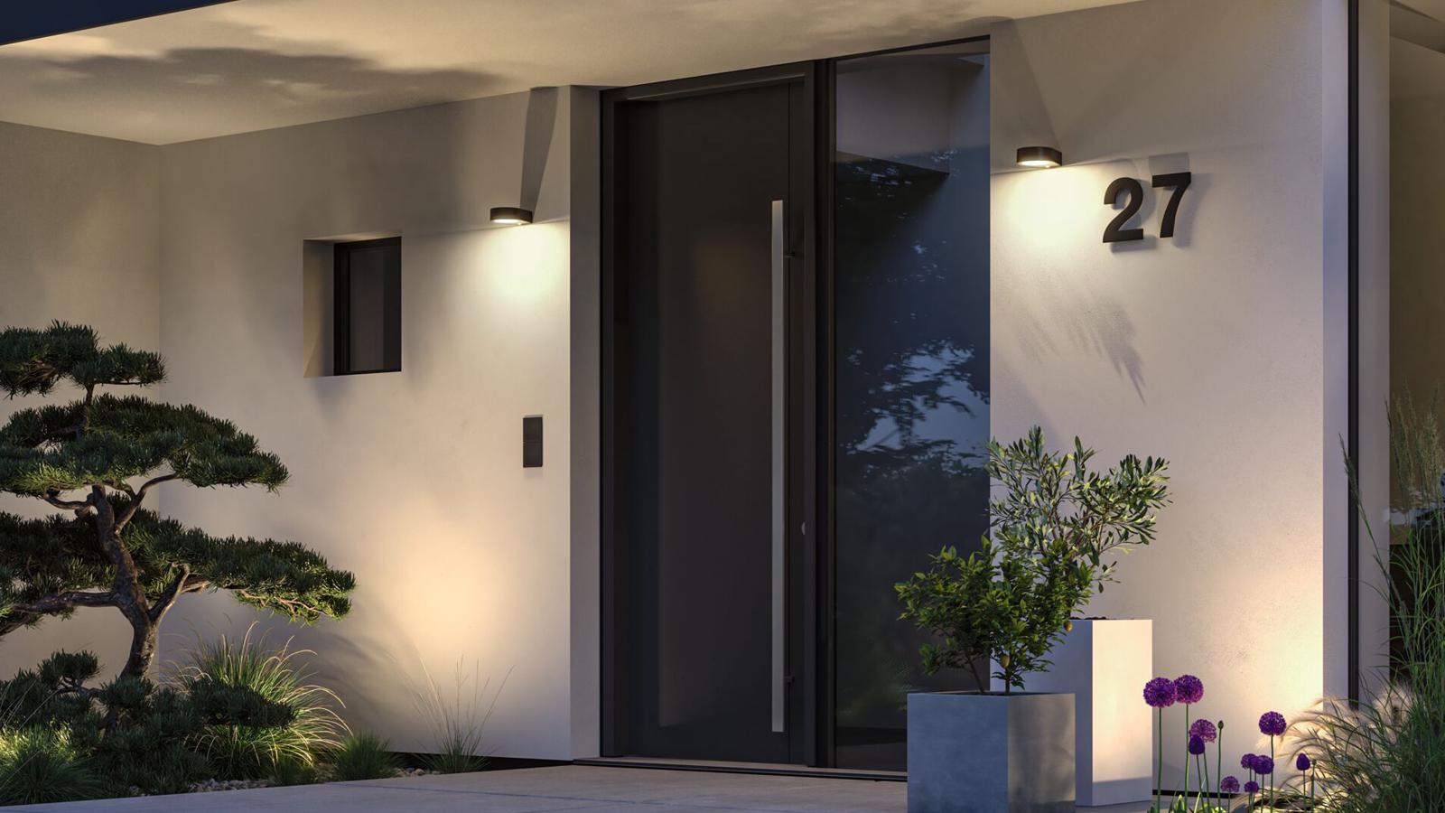 Moderne Außenwandleuchten in Schwarz beleuchten Eingangsbereich mit Hausnummer und Pflanzen bei Nacht.