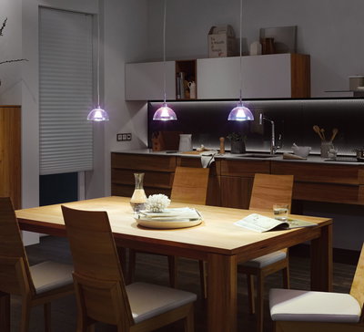 Cuisine moderne avec table en bois et trois suspensions LED en verre transparent diffusant une lumière blanche.