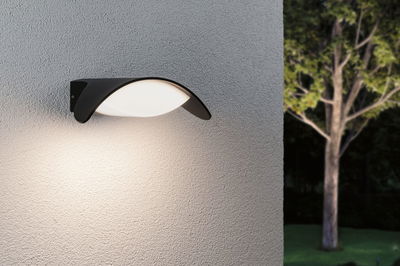 Modern black outdoor wall light with white diffuser on grey wall, garden lighting at night