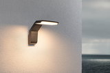 Moderne anthrazitfarbene LED-Außenwandleuchte an weißer Wand mit warmweißem Licht und Meerblick