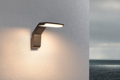 Moderne anthrazitfarbene LED-Außenwandleuchte an weißer Wand mit warmweißem Licht und Meerblick