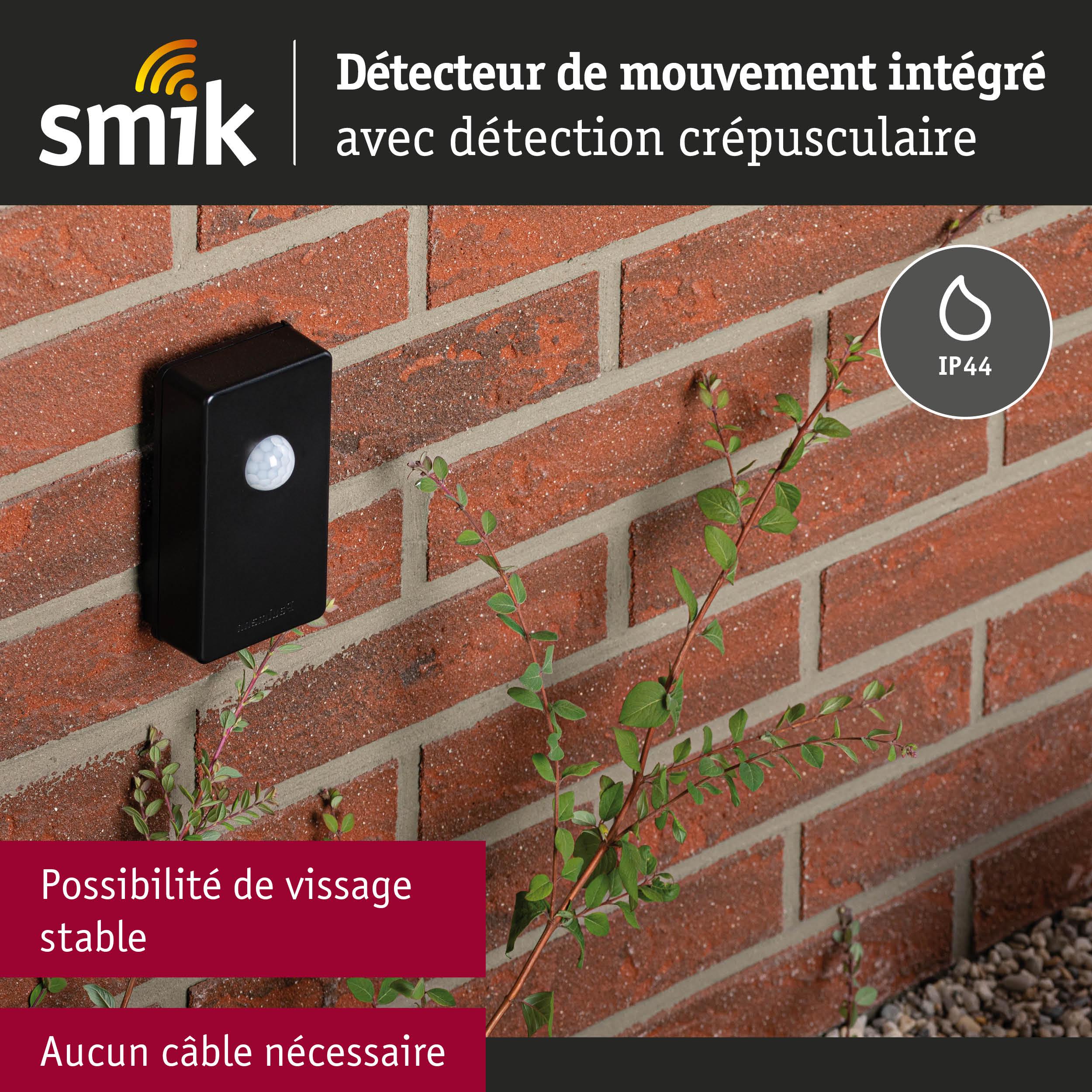 Détecteur de mouvement noir en plastique fixé sur mur en brique rouge avec protection IP44