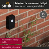 Détecteur de mouvement noir en plastique fixé sur mur en brique rouge avec protection IP44