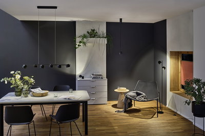 Modernes Esszimmer mit schwarzer Pendelleuchte und Stehleuchte aus Metall, Holzfußboden und dunklen Wänden