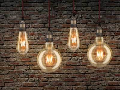 Four gold pendant lights with warm glow hanging in front of red brick wall, decorative indoor lighting.