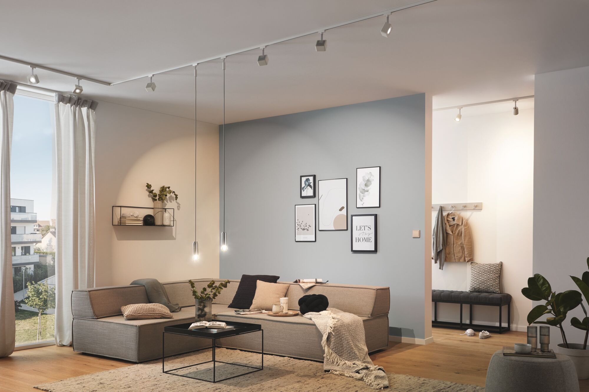 Modernes Wohnzimmer mit grauem Ecksofa, schwarzen Hängeleuchten und minimalistischer Wanddeko, Holzfußboden.