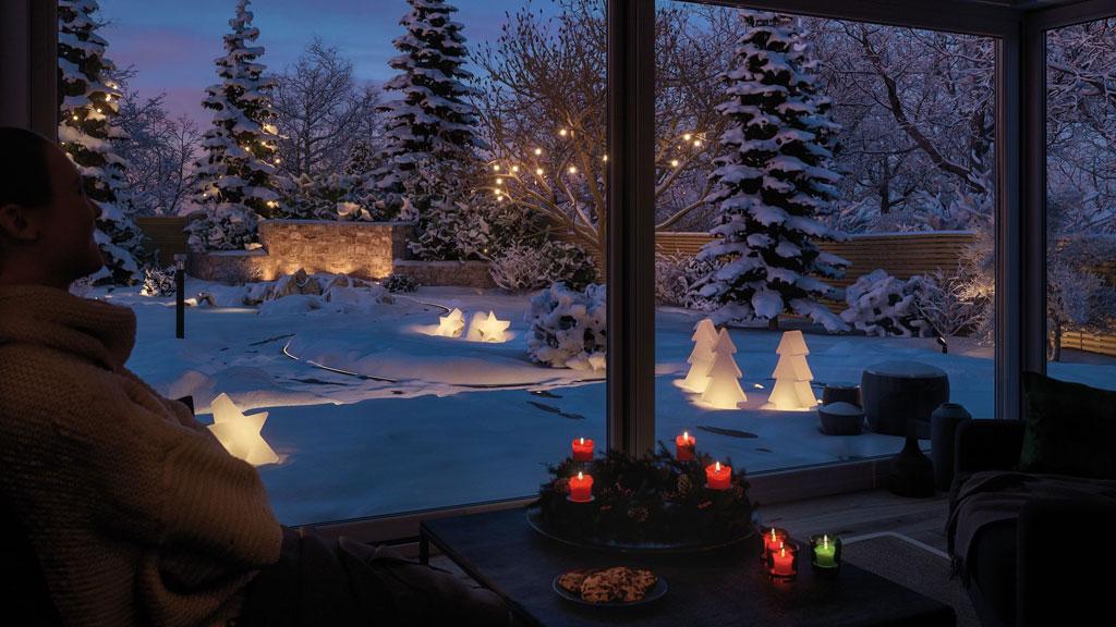 Winter garden with candles and LED star and tree-shaped decorative lights in snowy garden at dusk
