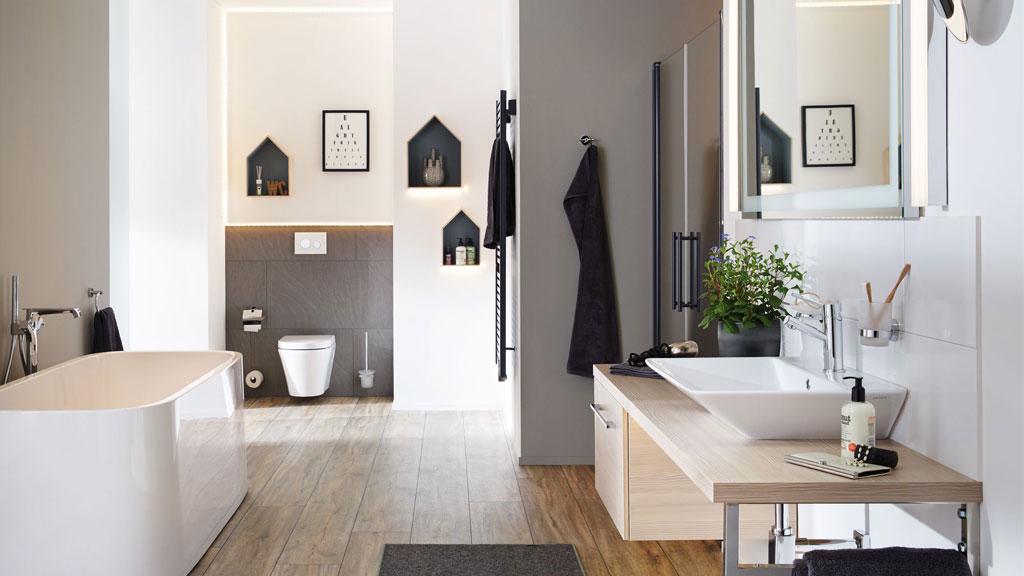 Modern bathroom with freestanding bathtub, illuminated mirror, and wooden countertop with white sink.