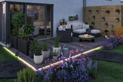 Modern terrace with LED floor lighting, grey rattan seating and colorful garden flowers in evening light.