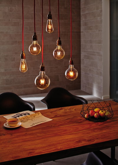 Zes hangende vintage gloeilampen met rode snoeren boven houten tafel met fruitmand en kopje.