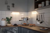Cuisine moderne avec machine à expresso en acier inoxydable, plan de travail en bois et éclairage LED blanc chaud.
