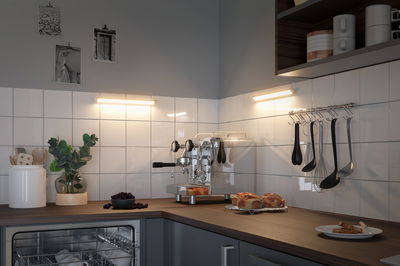 Cuisine moderne avec machine à expresso en acier inoxydable, plan de travail en bois et éclairage LED blanc chaud.