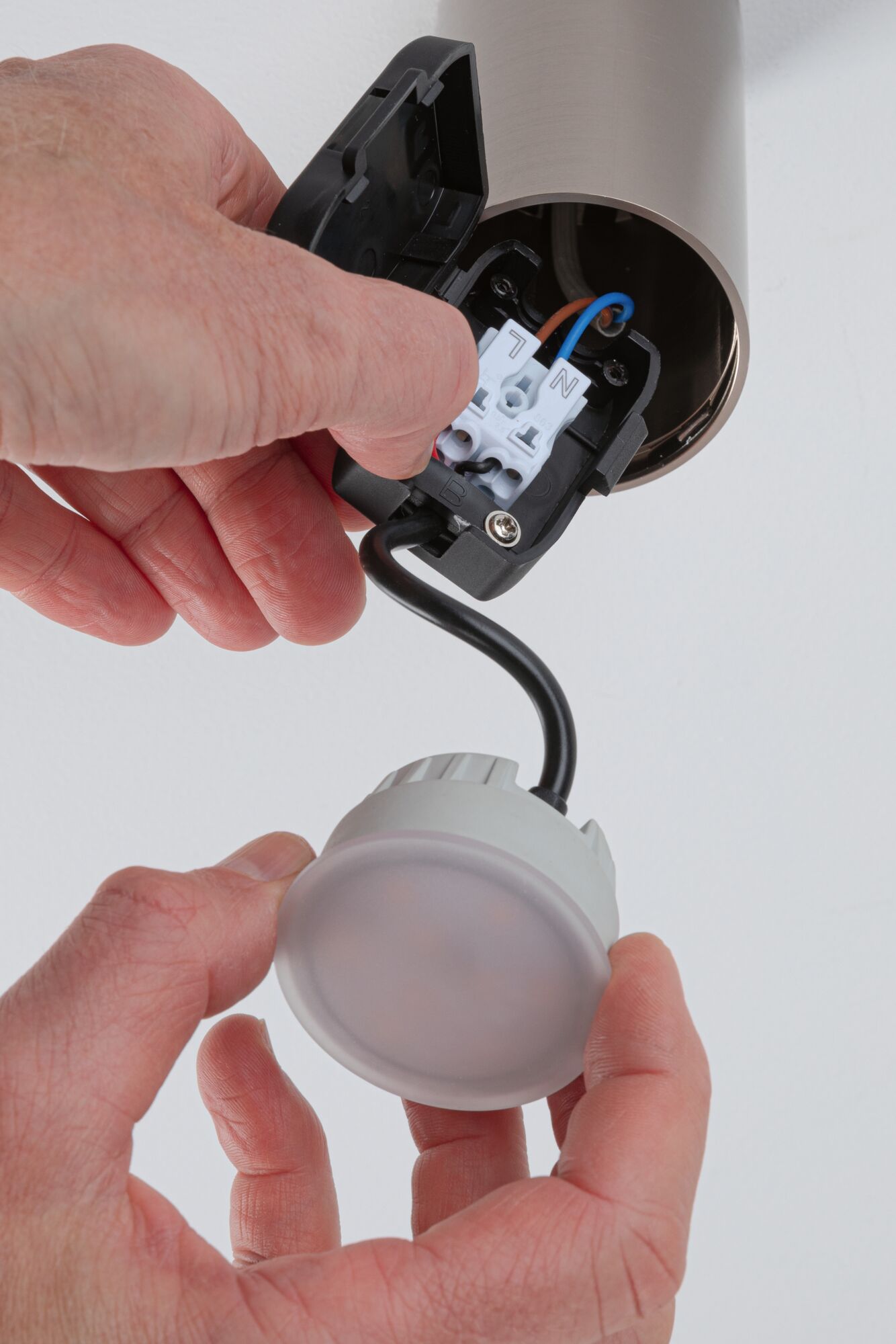 Main installant un plafonnier LED rond avec boîtier en plastique blanc et câble noir