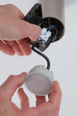 Main installant un plafonnier LED rond avec boîtier en plastique blanc et câble noir