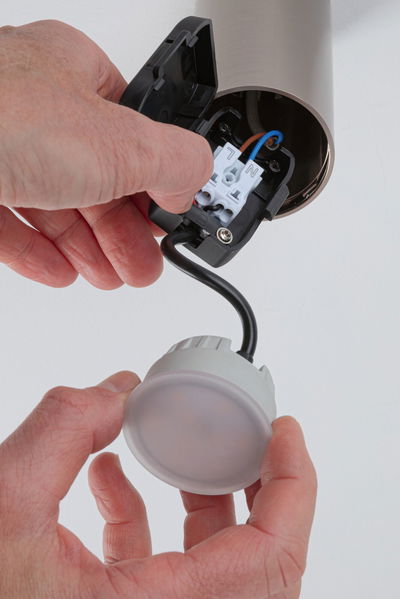 Main installant un plafonnier LED rond avec boîtier en plastique blanc et câble noir