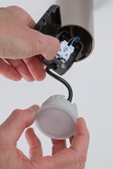 Hand installing round LED ceiling light with white plastic housing and black cable connection